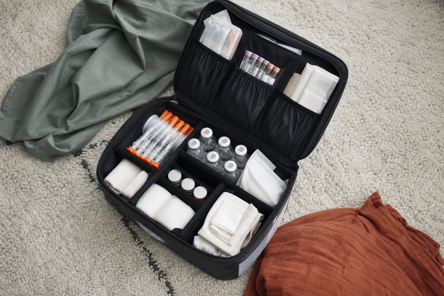 Open midwife supply case on a cream rug with neatly organized vials, syringes, and gauze
